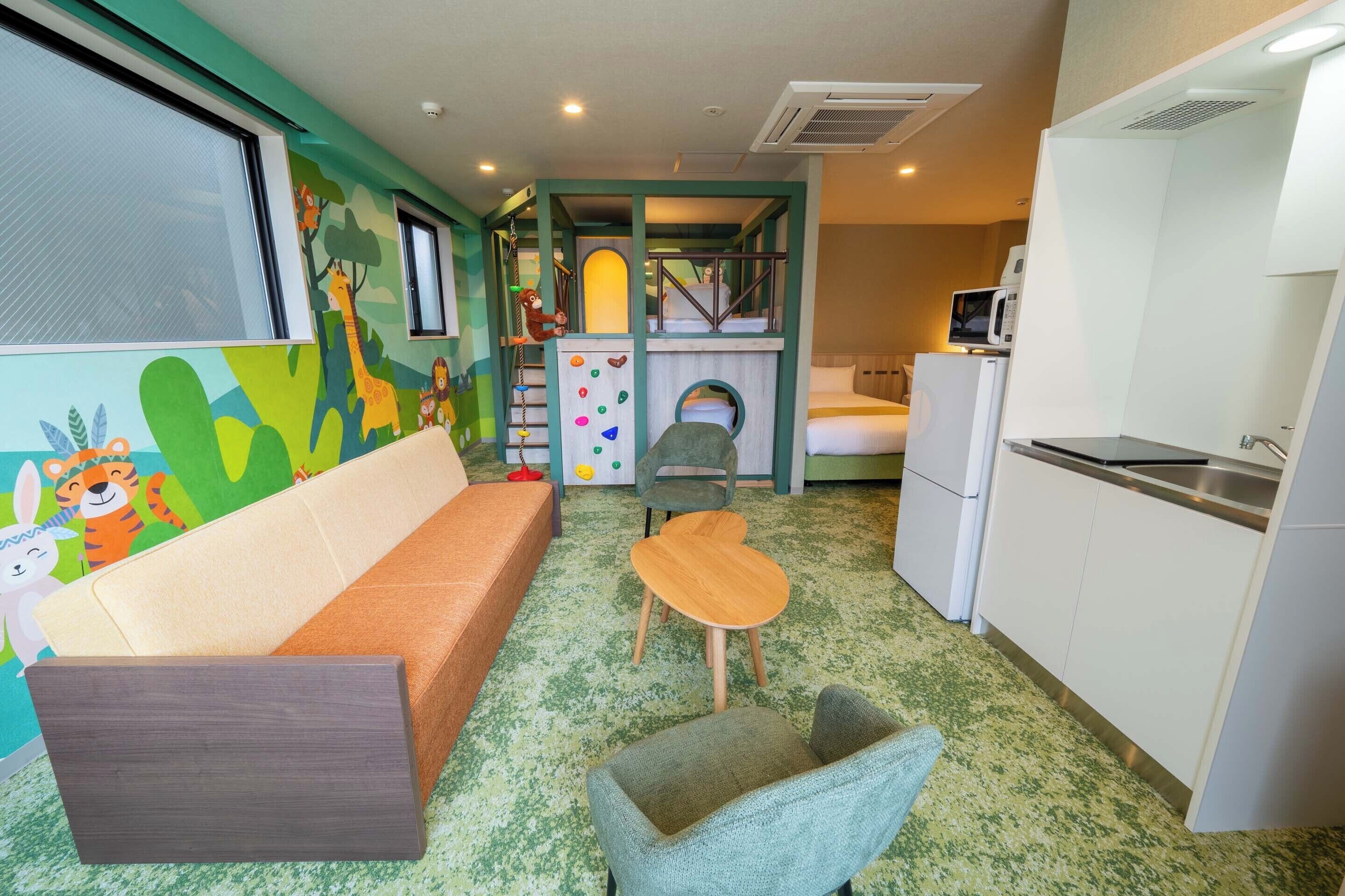 Zona de juegos infantiles con tobogán, pared de escalada y un espacio pequeño y cerrado. Hay un sofá, una mesita y una kitchenette con microondas.