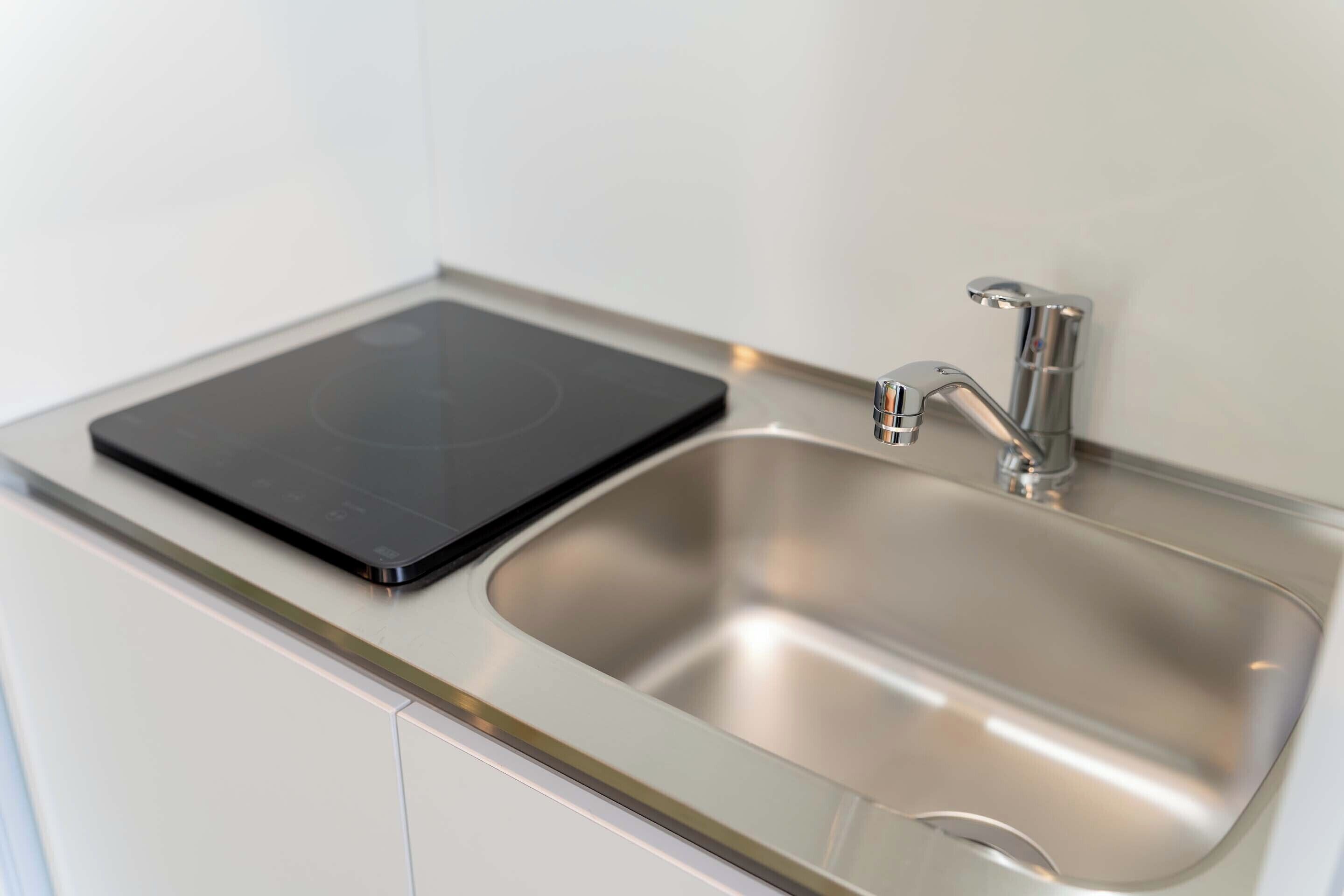 A stainless steel sink with a modern faucet and a black induction cooktop on a white countertop.