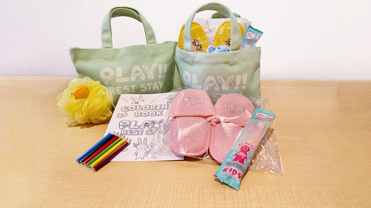 Una mesa con un libro para colorear, pantuflas rosas, una bata amarilla, una bolsa de tela verde y un patito de juguete.
