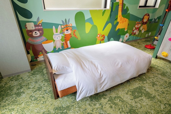 Una cama pequeña con ropa de cama blanca en una habitación con alfombra verde y un mural en la pared con animales y motivos naturales.