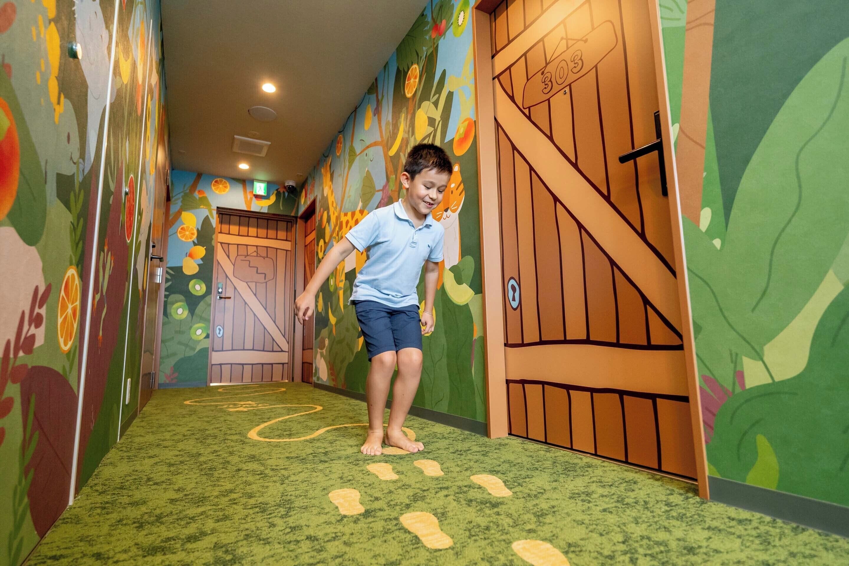 A child walking on a carpeted hallway with colorful murals and a wooden door.