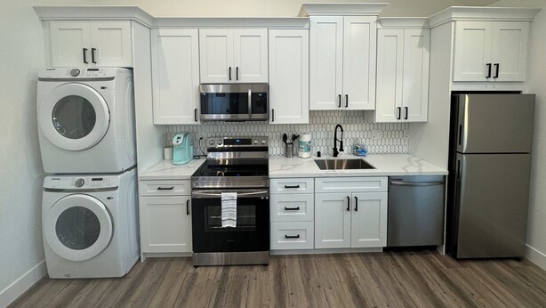 A modern kitchen with white cabinets, stainless steel appliances, and a wooden floor.