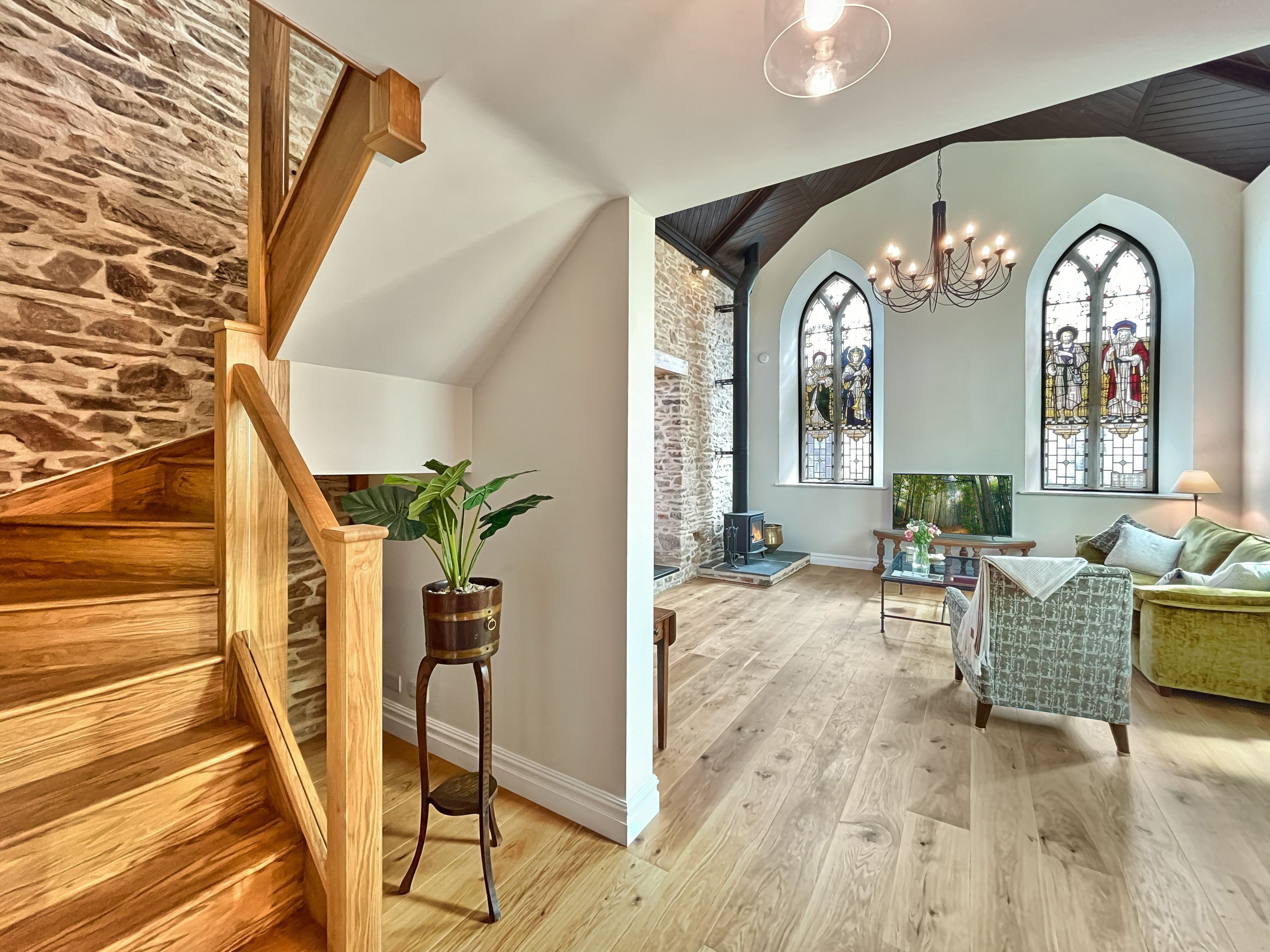 A spacious living area with a wooden staircase, stone wall, and a cozy fireplace.