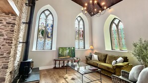A spacious room with a stone wall, wooden ceiling, and large stained glass windows. - The Chapel, Brompton Regis (Dulverton)