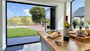 A modern kitchen with a large window offering a view of a green lawn and a tree. - The Chapel, Brompton Regis (Dulverton)