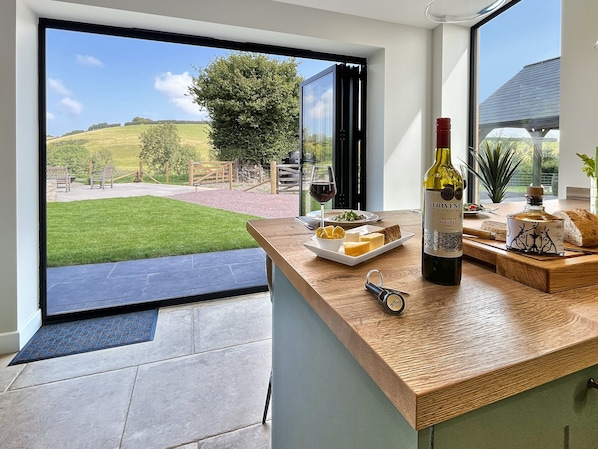 A modern kitchen with a large window offering a view of a green lawn and a tree. - The Chapel, Brompton Regis (Dulverton)