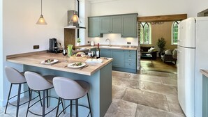 A modern kitchen with a large island, bar stools, and a dining area. - The Chapel, Brompton Regis (Dulverton)