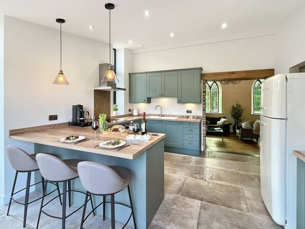 A modern kitchen with a large island, bar stools, and a dining area. - The Chapel, Brompton Regis (Dulverton)