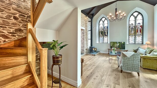 A spacious living area with a wooden staircase, stone wall, and a cozy fireplace. - The Chapel, Brompton Regis (Dulverton)