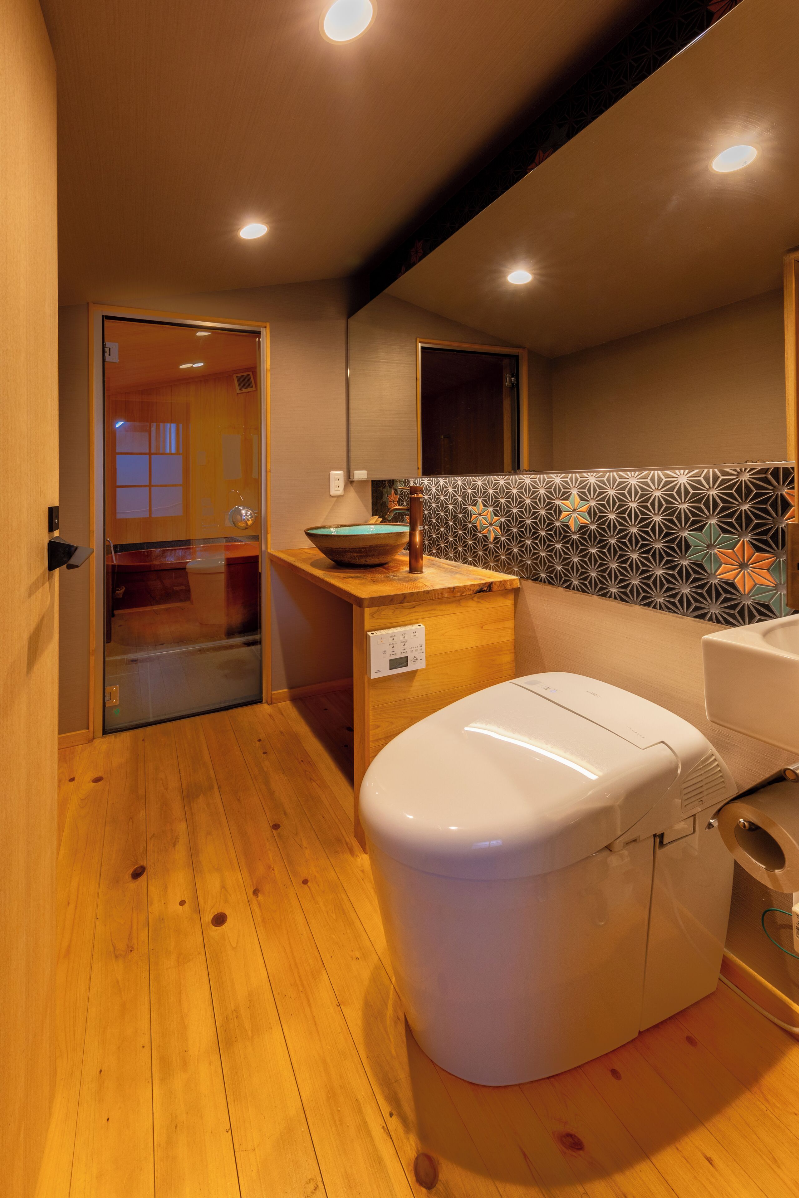 A compact bathroom with a wooden floor, a white toilet, a sink, and a decorative backsplash.