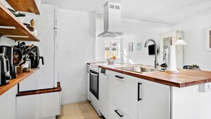 Een moderne keuken met witte kastjes, een houten aanrecht, een ingebouwde oven en een roestvrijstalen spoelbak.