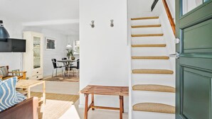 Een moderne woonkamer met een houten bank, een eethoek met een tafel en stoelen, en een trap met een groene deur.