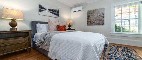 A bedroom with a bed, two bedside tables with lamps, a window with a view, and artwork on the walls.