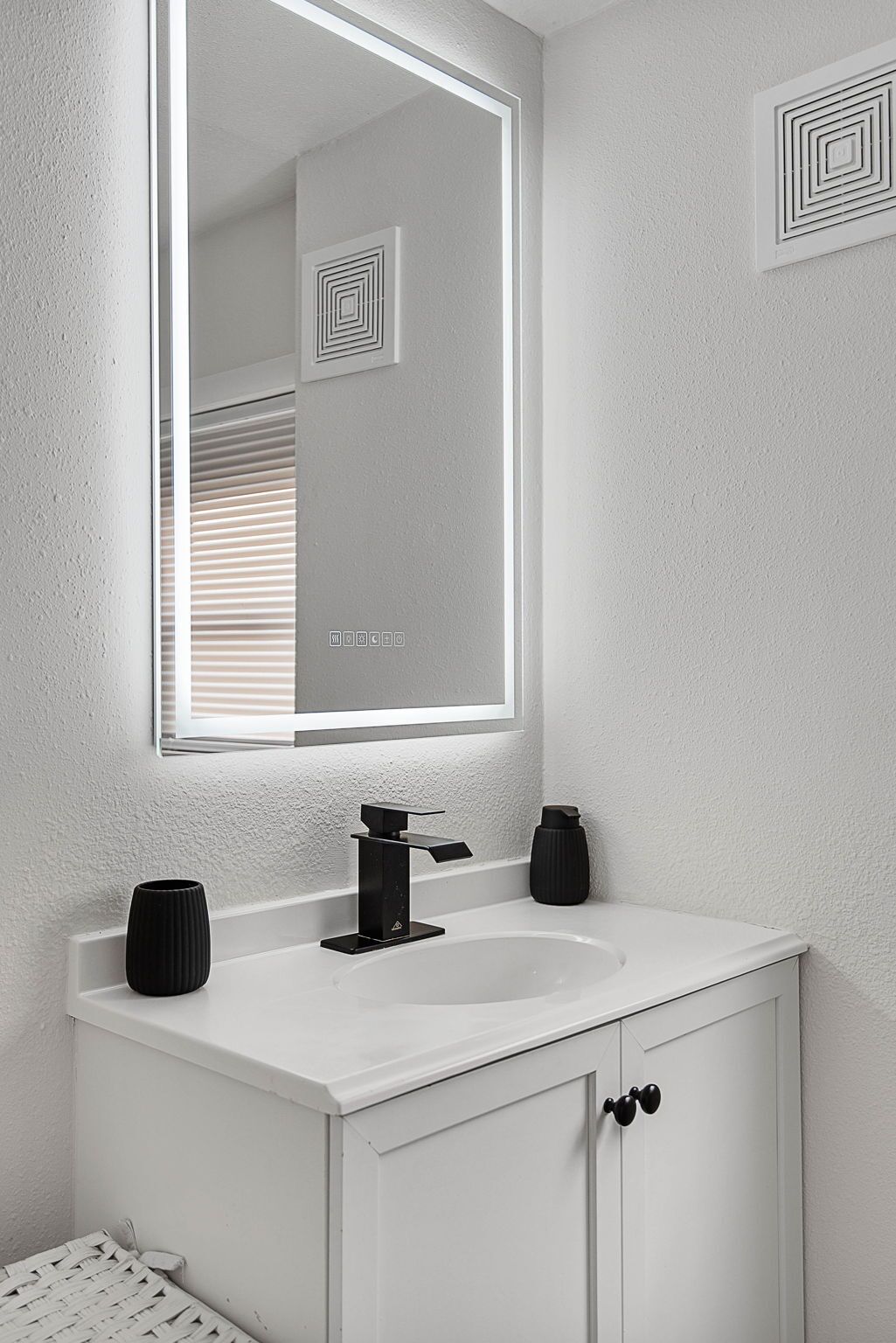 Een badkamer met een witte wastafel, een zwarte kraan en een spiegel met verlichting rondom.