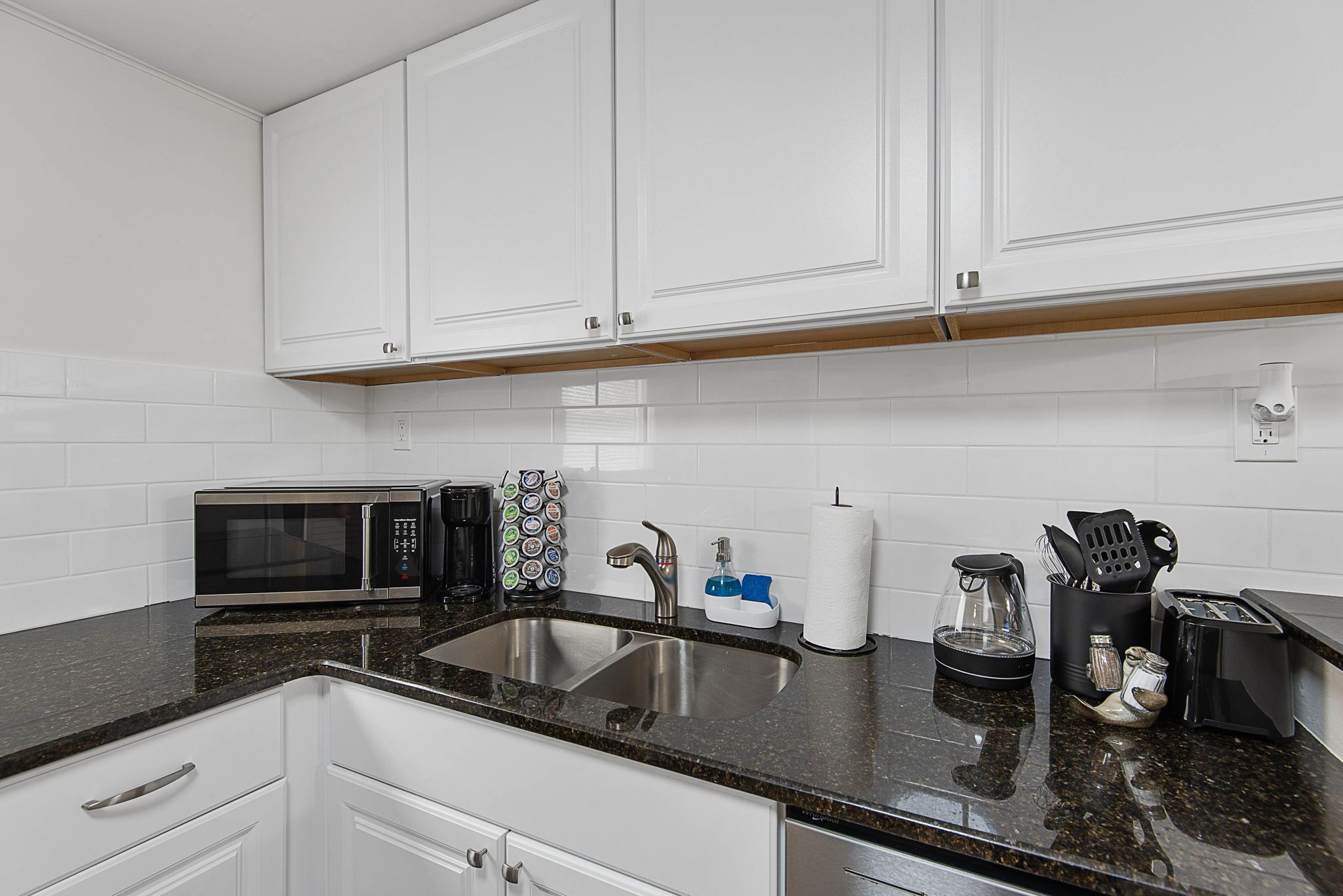 A kitchen with white cabinets, a stainless steel sink, a microwave, a coffee maker, and a toaster.
