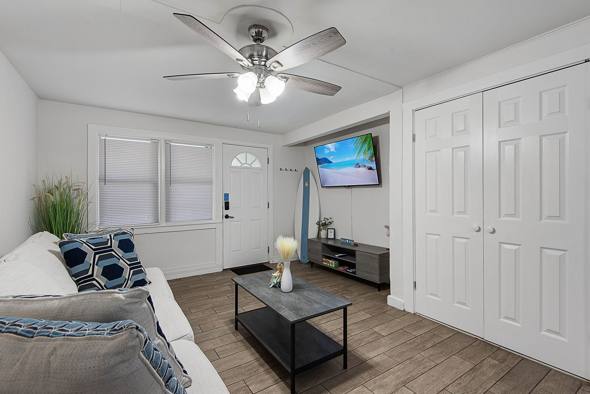 A living room with a ceiling fan, a television, a sofa, a coffee table, and a door.