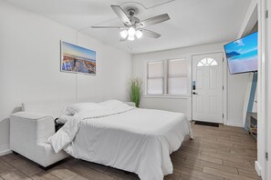 A bedroom with a bed, a ceiling fan, a TV, and a window with blinds.