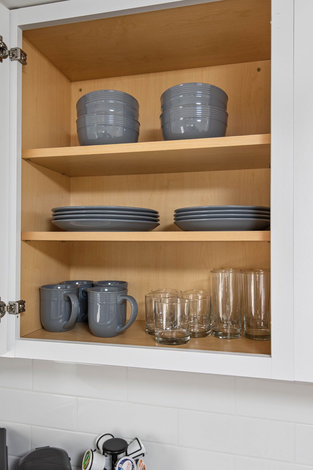 Un meuble de cuisine avec des étagères où sont rangées des assiettes, des bols et des verres.