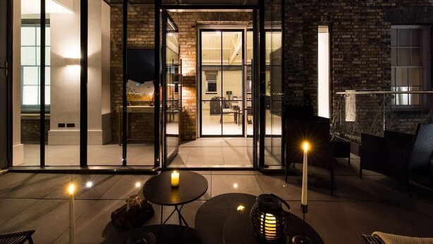 Un interior moderno con puertas de vidrio que dan a un comedor, una chimenea y una zona de estar con mesas y sillas.