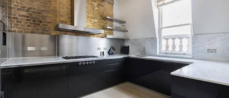 A modern kitchen with black cabinets, a stainless steel range hood, and a window providing natural light.