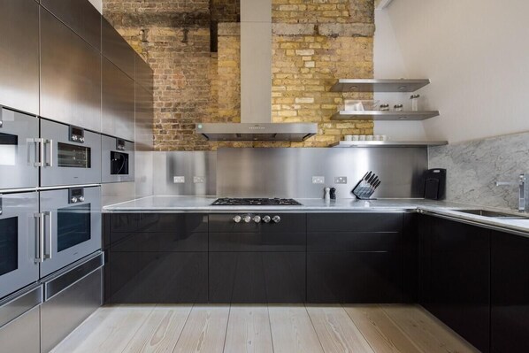 A modern kitchen with stainless steel appliances, a central island, and a brick wall.