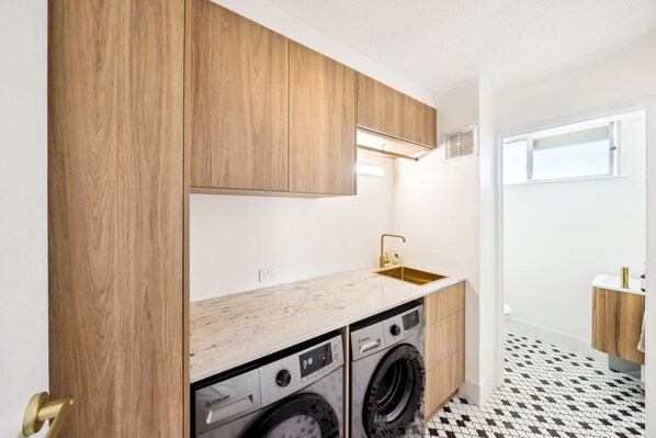 Una cucina compatta con mobili in legno, un lavello in acciaio inossidabile e lavatrice e asciugatrice integrate.