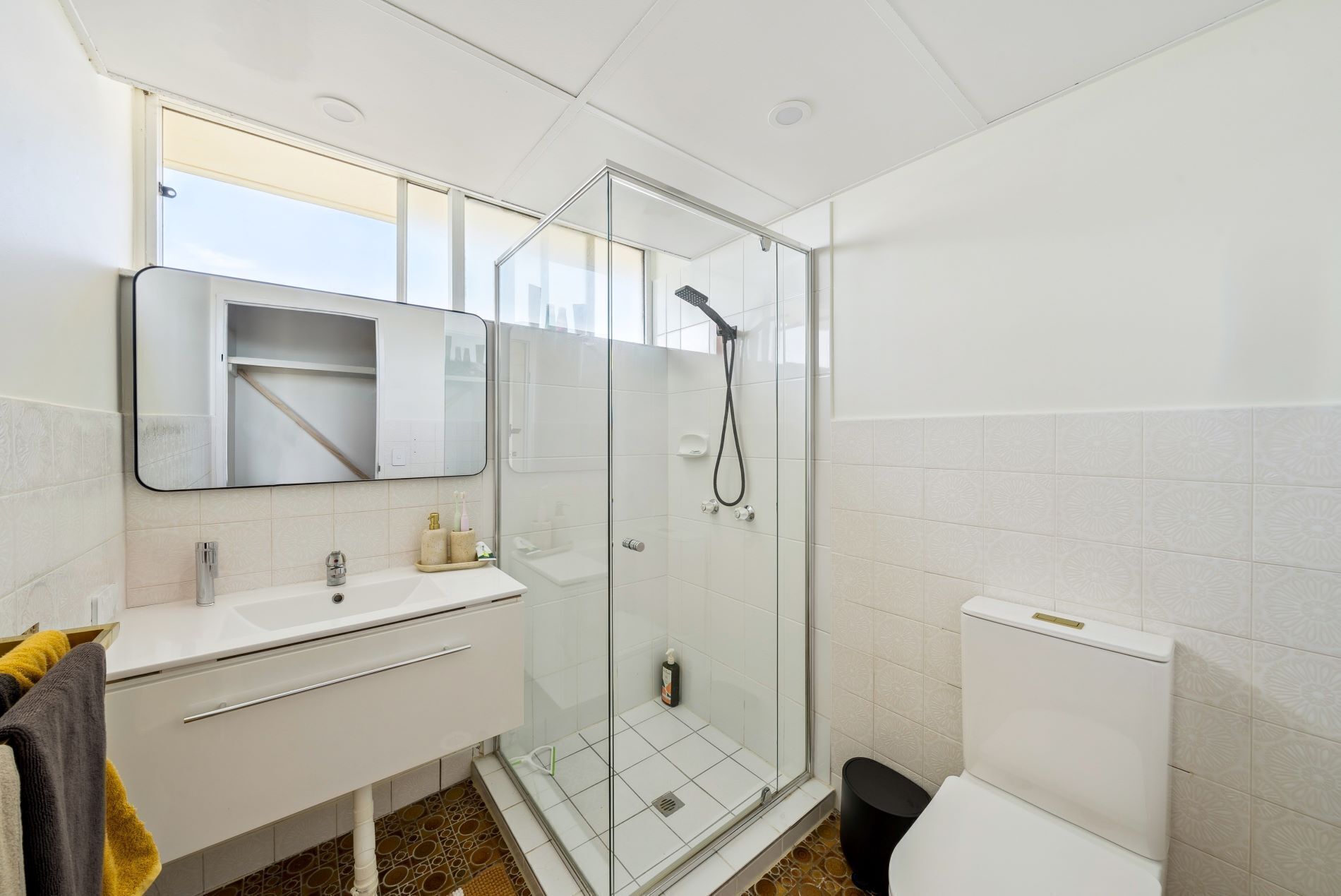 A modern bathroom with a glass-enclosed shower, a white sink with a mirror, and a toilet.
