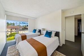 Una camera d'albergo con due letti, una grande finestra e vista su edifici e vegetazione.