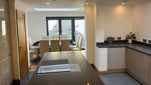 A modern kitchen with a central island, a dining area with chairs, a black countertop, and a potted plant. - Entire Seaside Home 6 Private Bedrooms Sleeps 10 (Wallasey)
