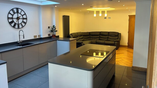 A modern kitchen with a central island, a built-in sink, and a wall-mounted clock. - Entire Seaside Home 6 Private Bedrooms Sleeps 10 (Wallasey)