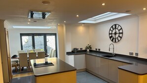 A modern kitchen with a central island, a dining area with chairs, and a large window. - Entire Seaside Home 6 Private Bedrooms Sleeps 10 (Wallasey)