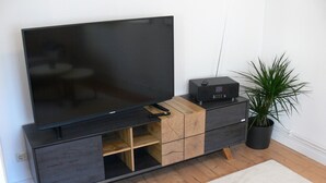 Televisor de pantalla plana sobre un mueble de madera y color negro, con control remoto y un altavoz pequeño.
