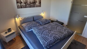 Un dormitorio moderno con una cama, mesitas de noche, una obra de arte en la pared y una lámpara colgante.