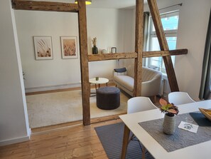 A modern interior with a wooden ceiling structure, a sofa, a dining table with a vase, and a view of a building outside.