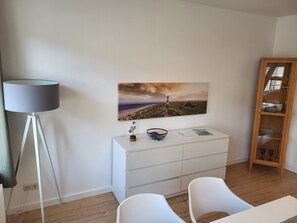 A modern room with a white dresser, a lamp, a painting, and a wooden cabinet.