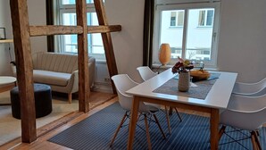 Un comedor moderno con una mesa de madera, sillas blancas, un banco acolchado y un jarrón con flores.