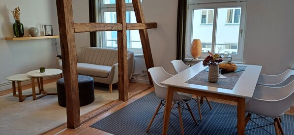 A modern dining area with a wooden table, white chairs, a cushioned bench, and a vase with flowers.