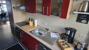 Una cocina moderna con armarios rojos, un lavamanos de acero inoxidable, una cafetera y una tabla de cortar de madera.