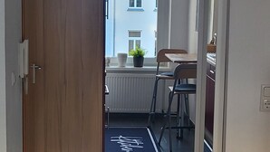 Un pasillo con puerta de madera, un radiador, una planta en maceta, una silla y una mesa.
