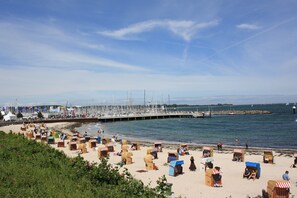 Una playa con numerosas cabañas y un muelle con veleros.