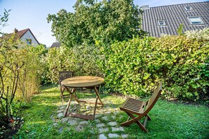 A garden with a wooden table and chairs, surrounded by lush greenery and a hedge.