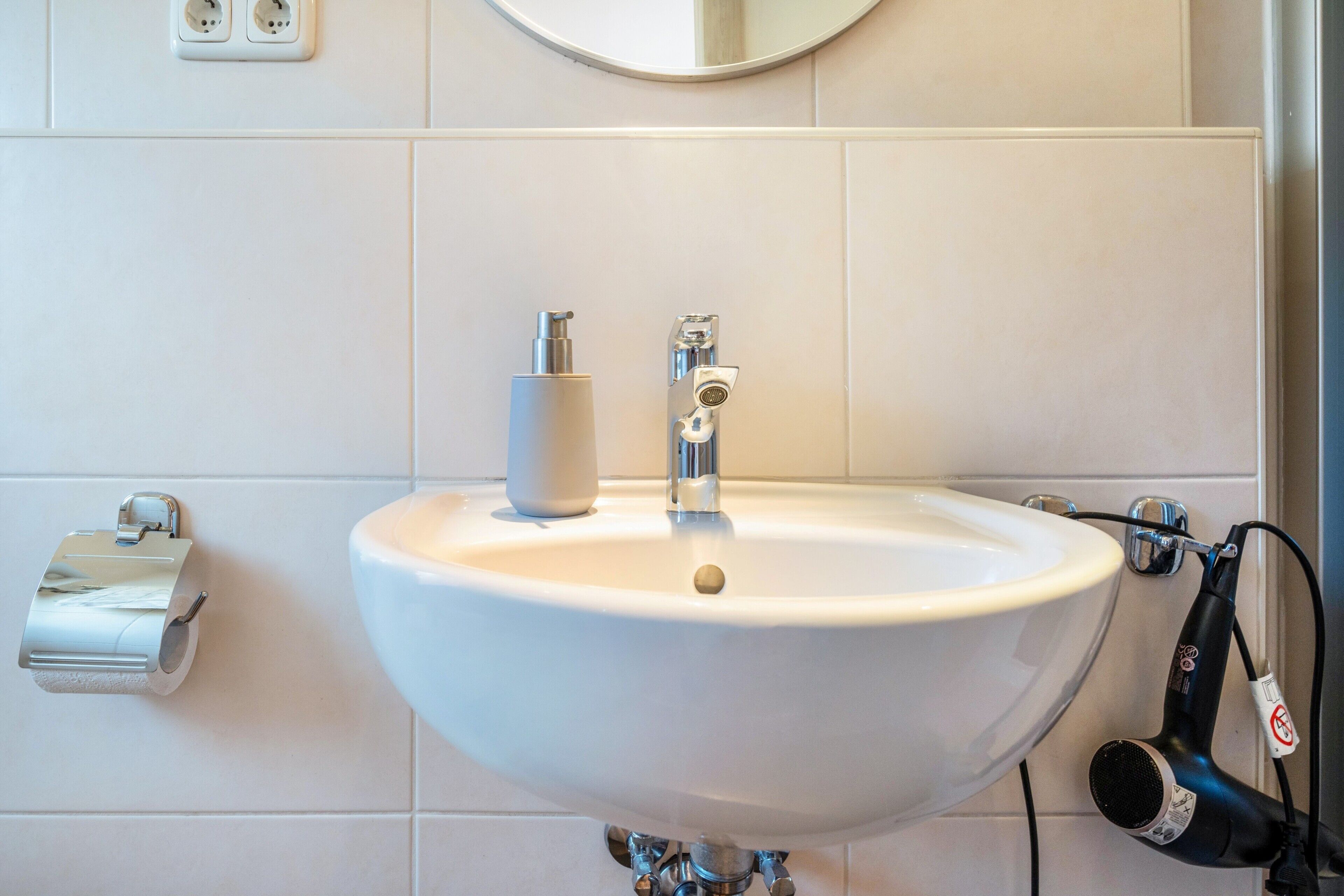A bathroom with a white sink, a toilet paper holder, and a hairdryer plugged in.