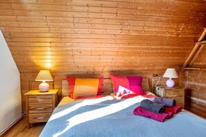Une pièce aux murs lambrissés, comprenant un lit, deux tables de chevet, une lampe et une fenêtre.