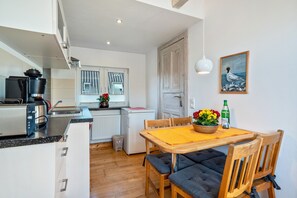 A compact kitchen with modern appliances, a dining area with a wooden table and chairs, and a view of the adjacent room. - Apartment 'Öko Fewo Lachmöwe' with Balcony and Wi-Fi (Kiel)