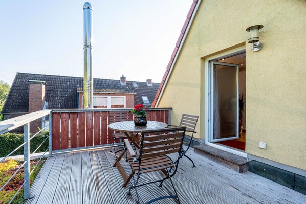 A wooden deck with a round table and chairs, a potted plant, and a sliding glass door leading to an interior space.