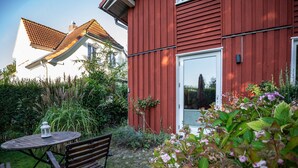 Un edificio rojo con una puerta blanca, un jardín con plantas y una mesa con un banco.