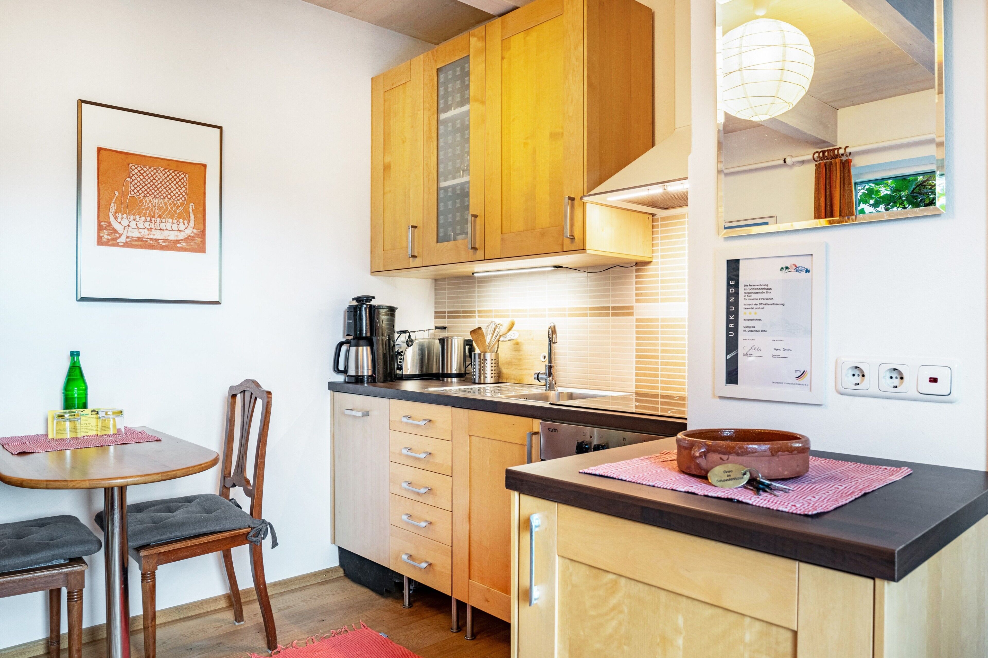 A compact kitchen with wooden cabinets, a dining table with chairs, a coffee maker, and a kettle.
