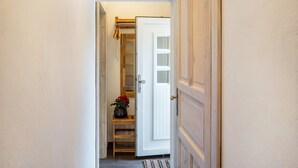 A narrow hallway with a wooden door, a small table with a vase, and a shelf with folded clothes.
