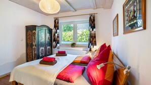 A bedroom with a bed, a window with curtains, a radiator, and a wooden cabinet.