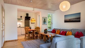 A modern living space with a grey sofa, wooden dining table, and a kitchen in the background.